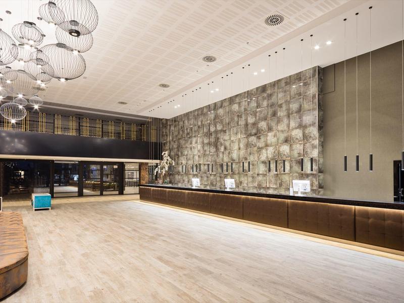 Ampia hall d'hotel con illuminazione moderna, parete in pietra e banco reception in legno.