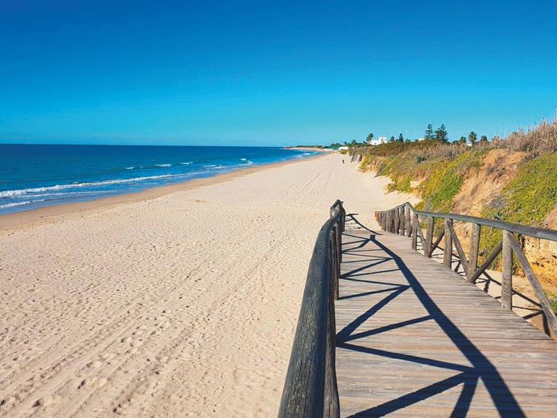 Spiaggia di sabbia con passerella in legno e corrimano sotto un cielo azzurro limpido