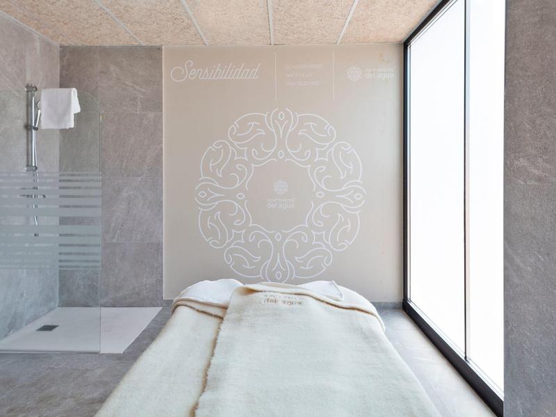 Sala spa minimalista con lettino da massaggio e grande finestra che fa entrare la luce naturale