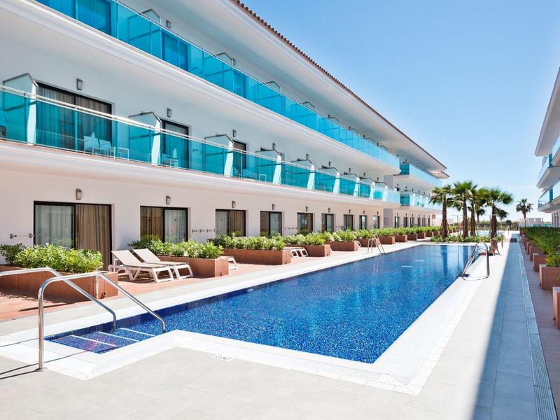 Area piscina moderna dell'hotel con lettini e balconi in vetro in una giornata di sole.