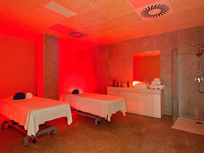 Sala spa con due letti da massaggio, luce rossa soffusa e area doccia.