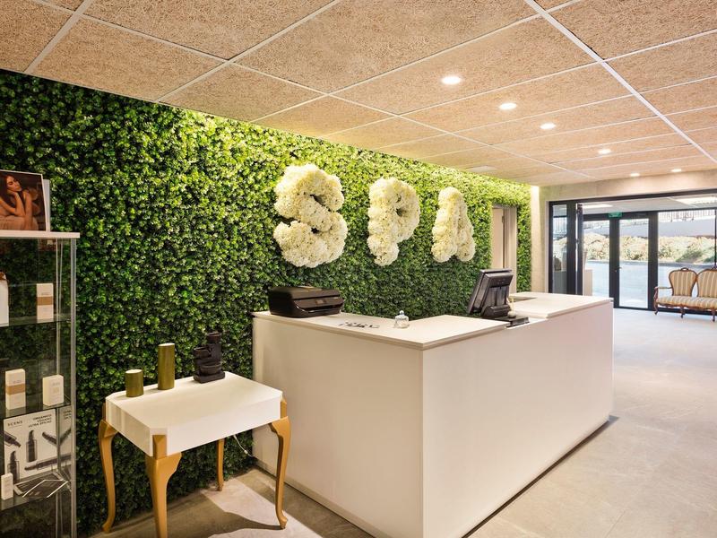 Reception spa moderna con parete verde di piante e banco bianco