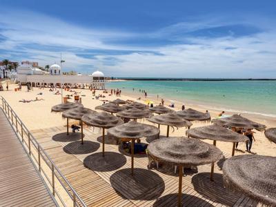 Muelle de madera con varias sombrillas de paja en la playa de arena con mar y cielo azul.