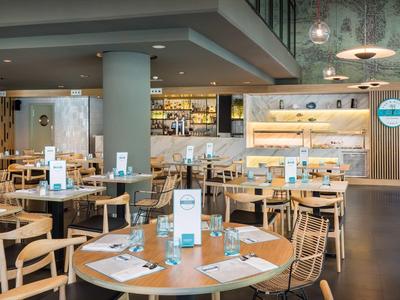 Restaurante moderno con muebles de madera, mesa redonda y iluminación elegante en ambiente cálido.