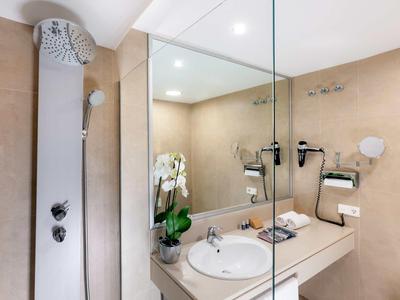 Baño moderno con ducha, lavabo, espejo grande y decoración con orquídeas blancas.