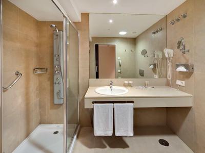 Baño luminoso con ducha, lavabo, espejo y toallas blancas.