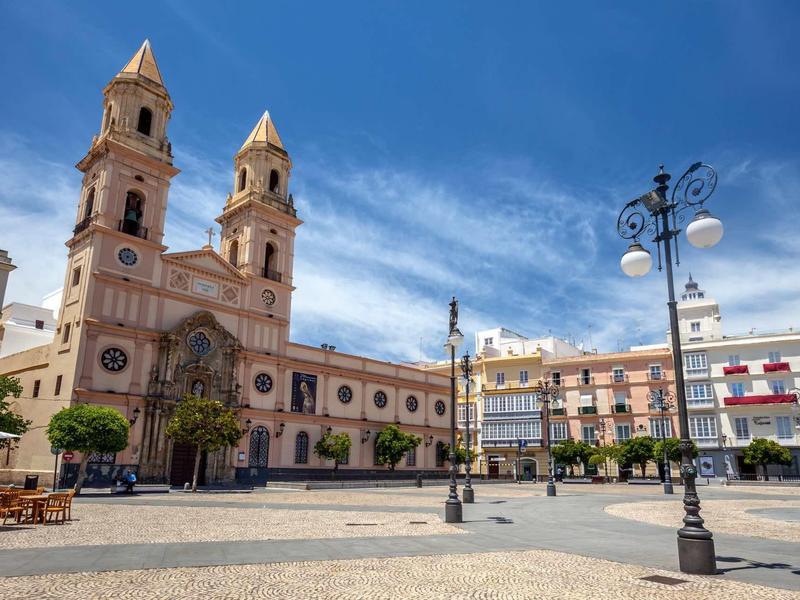 Iglesia histórica y edificios circundantes en una plaza soleada con cielo azul.