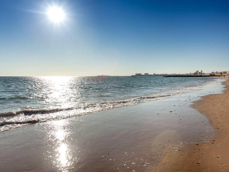 Playa con olas suaves, cielo claro y sol brillante en el horizonte.