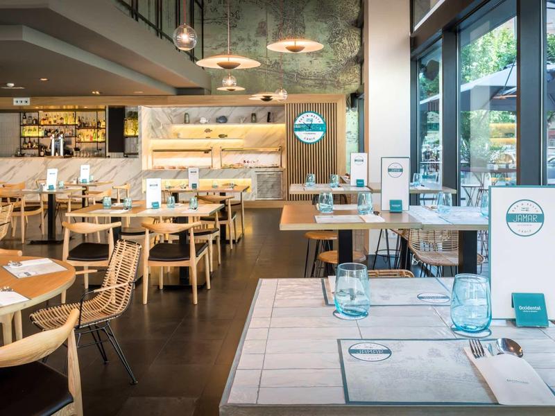 Restaurante moderno de hotel con muebles de madera clara y grandes ventanas con vista al exterior.