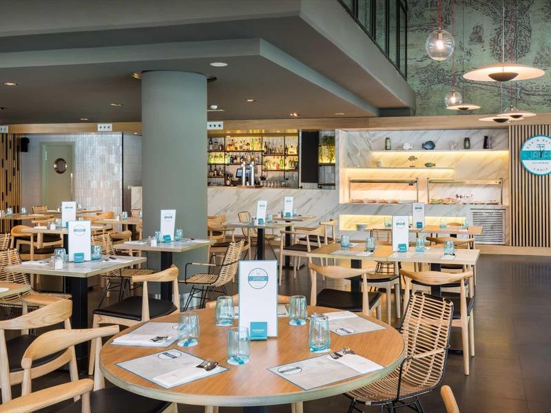 Restaurante moderno con muebles de madera, mesa redonda y iluminación elegante en ambiente cálido.