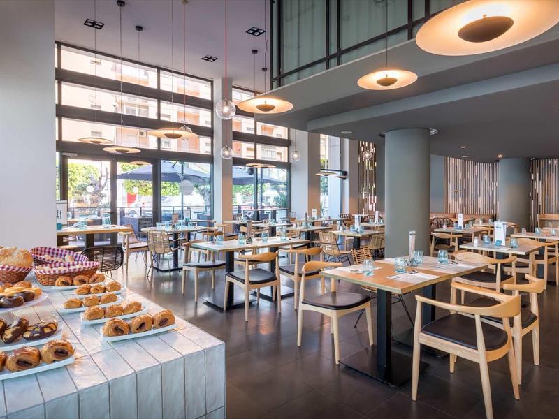 Restaurante moderno con mesas de madera, gran ventanal y una estación con bollería fresca