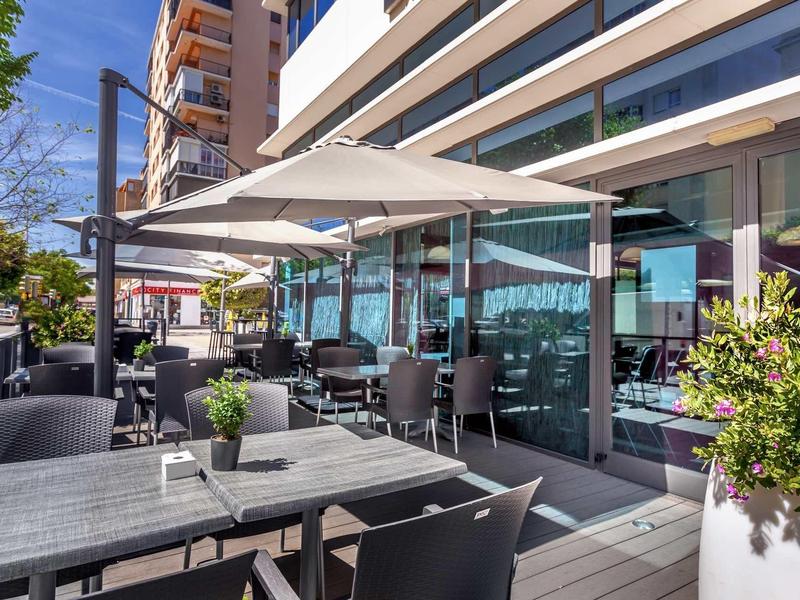 Terraza exterior moderna de un hotel con mesas, sillas y sombrillas en la ciudad.