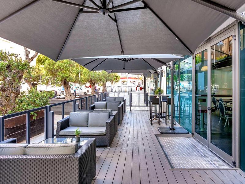 Terraza moderna de hotel con muebles grises y grandes sombrillas a la luz del día.