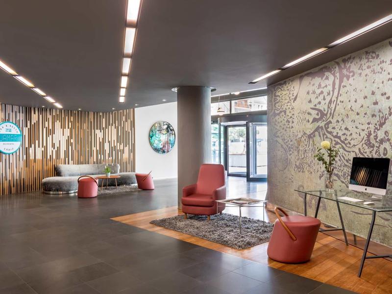 Moderna recepción de hotel con áreas de estar, suelo oscuro y pared decorativa de madera.