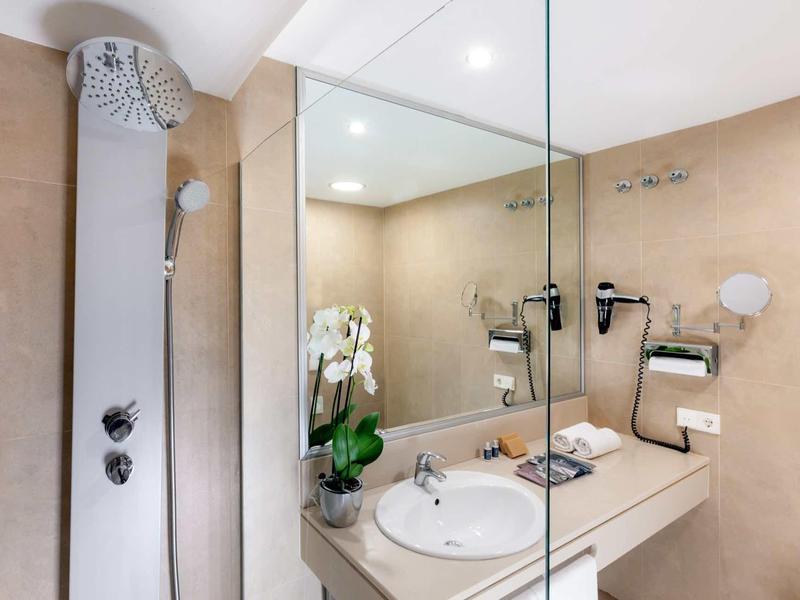 Baño moderno con ducha, lavabo, espejo grande y decoración con orquídeas blancas.