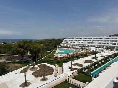 Hotel mit Swimmingpools, Liegestühlen und Palmen, umgeben von Grün mit Blick aufs Meer.