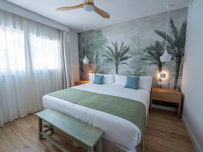 Helles Schlafzimmer mit großem Bett, botanischer Wandgestaltung und Holzfußboden.