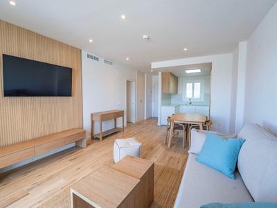 Modern eingerichtetes Wohnzimmer mit Sofa, Fernseher und Esstisch in hellem Raum.