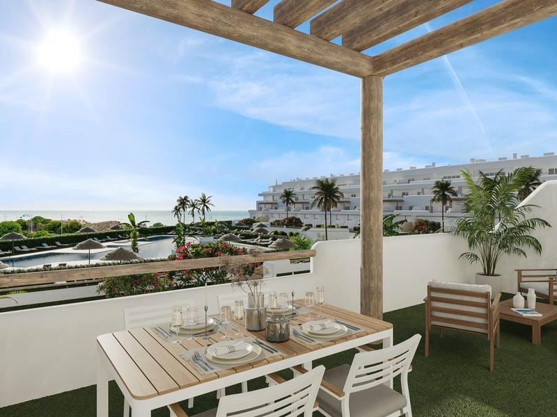 Terrasse mit Esstisch und Stühlen, Blick auf sonnige Uferpromenade mit Palmen und Wohnhäusern.