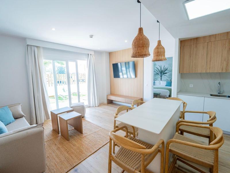 Helles Wohnzimmer mit Essbereich, Sofa, Holzmöbeln und großem Fenster mit Vorhängen.