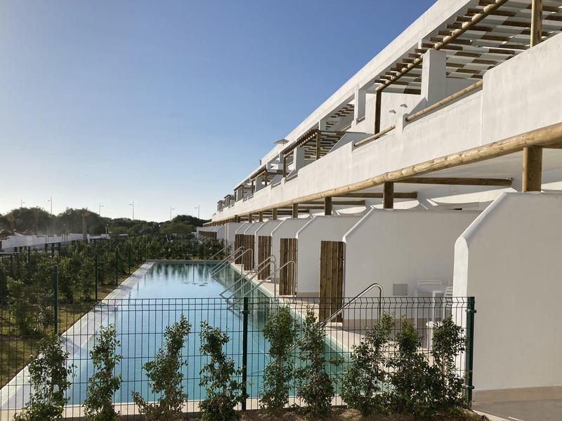 Modernes Hotel mit Pool, umgeben von grünen Pflanzen und klarem Himmel.
