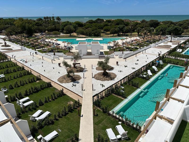 Luxuriöses Resort mit mehreren Pools, Liegestühlen und Blick auf das Meer im Hintergrund.