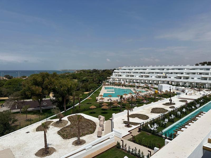 Hotel mit Swimmingpools, Liegestühlen und Palmen, umgeben von Grün mit Blick aufs Meer.