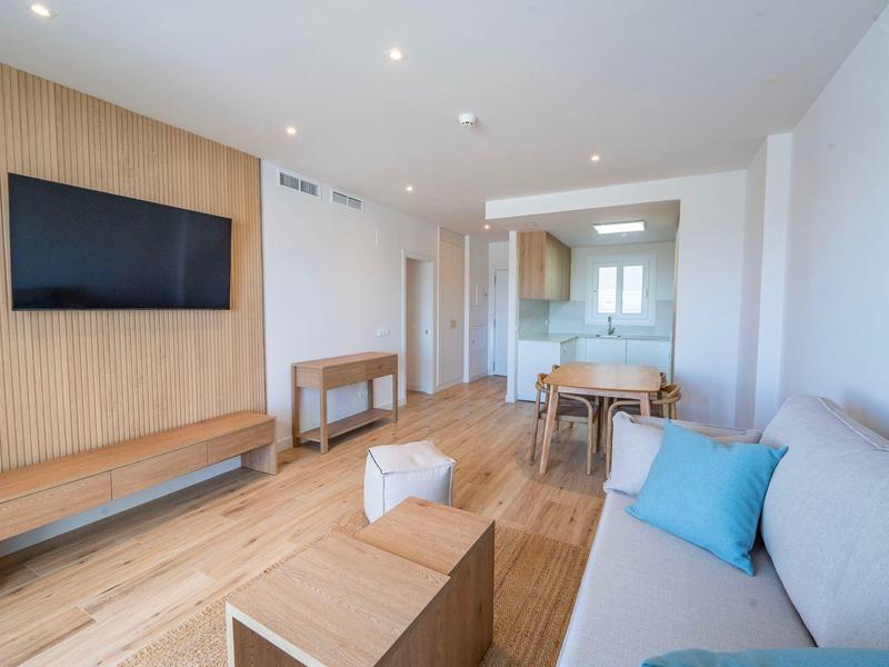 Modern eingerichtetes Wohnzimmer mit Sofa, Fernseher und Esstisch in hellem Raum.