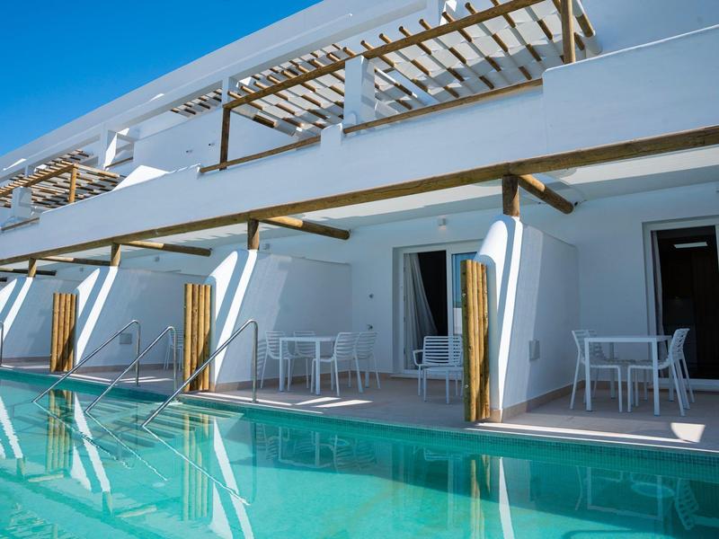 Moderner Hotelpool mit Terrasse, Stühlen und Tischen unter Pergolen bei klarem Himmel.