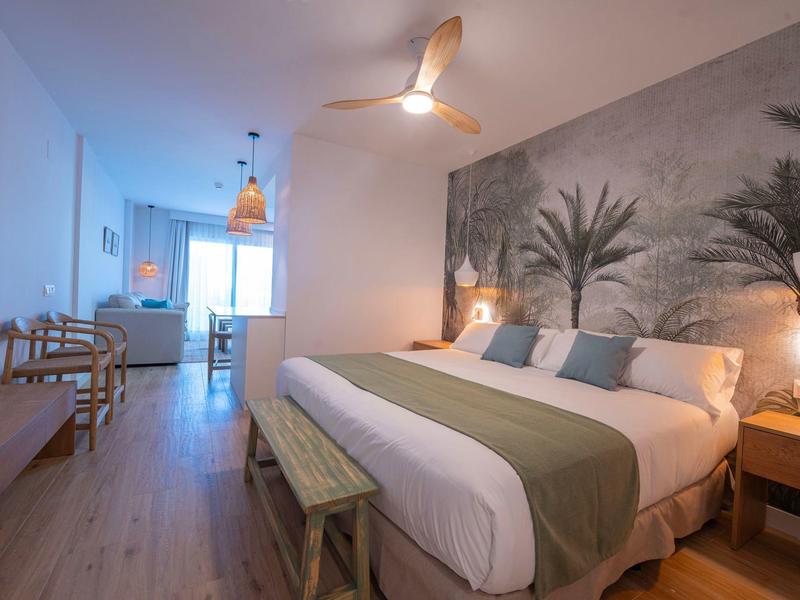 Modernes Hotelzimmer mit großem Bett, Palme-Wandbild und Holzboden.