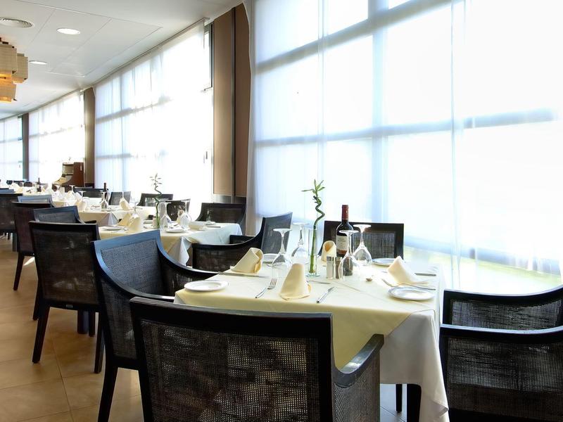 Světle osvětlená hotelová restaurace s bílými stolními dekoracemi a moderními židlemi.