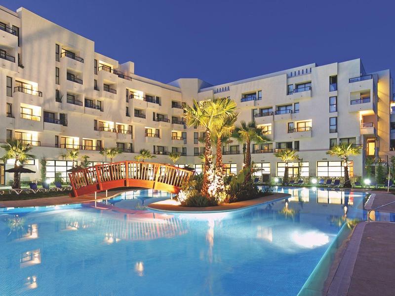 Moderní hotel s osvětleným venkovním bazénem a několika patry za soumraku