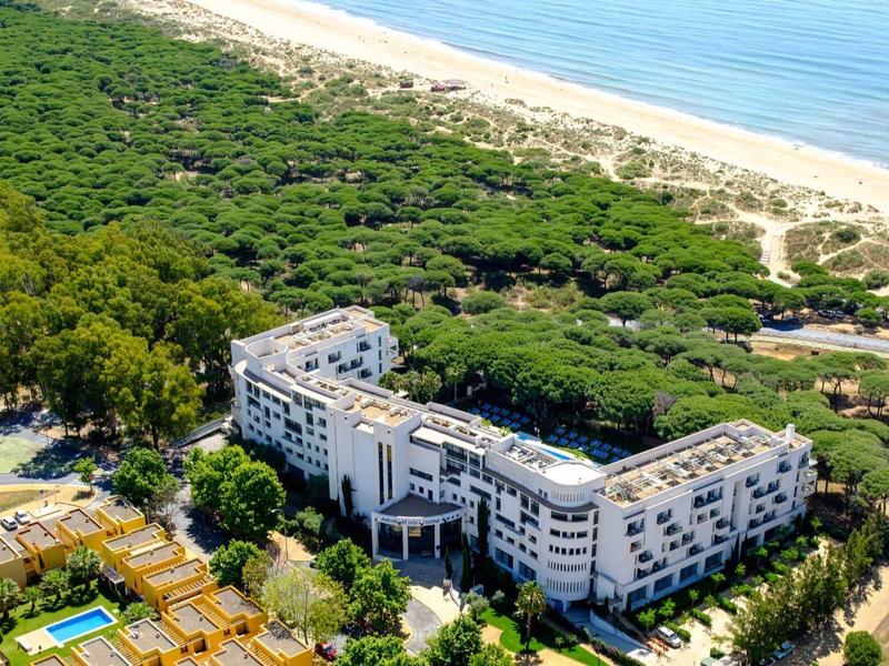 Velký hotel na okraji lesa vedle dlouhé písečné pláže a moře.