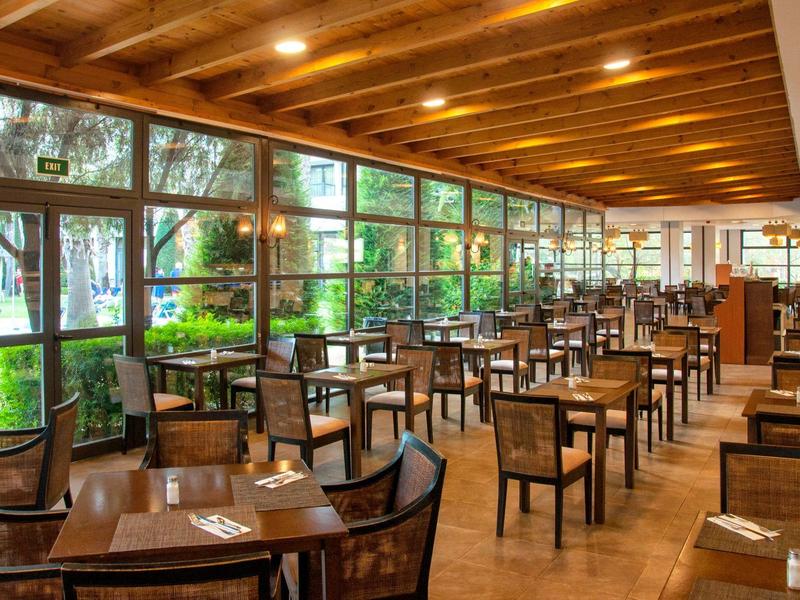 Prostorná jídelna s dřevěnými stoly, židlemi a velkými okny s výhledem do zahrady.