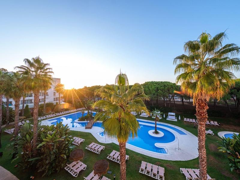 Hotelová bazénová plocha s lehátky a palmami při západu slunce.