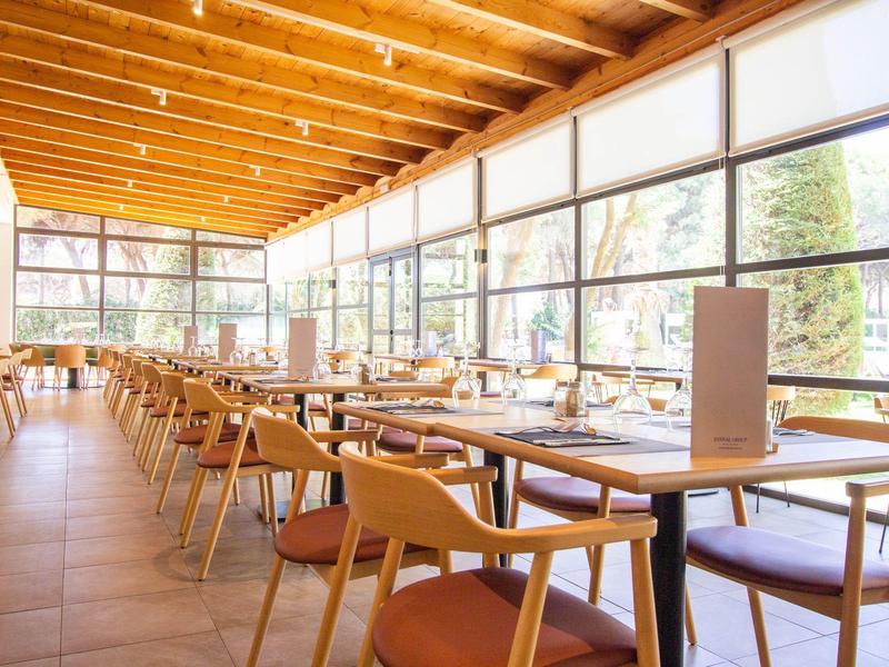 Světlá jídelna s dřevěným nábytkem a velkými okny vpouštějícími dostatek denního světla.