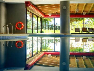 Piscina interior con columnas y grandes ventanales que dan a un paisaje verde exterior.