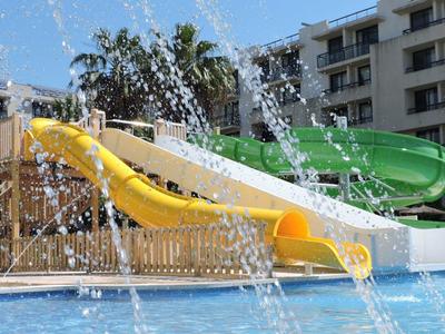 Toboganes de agua sobre una piscina con fuentes de agua frente a un edificio de hotel.