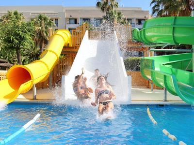 Niños deslizando por toboganes de agua coloridos hacia una piscina en un hotel.