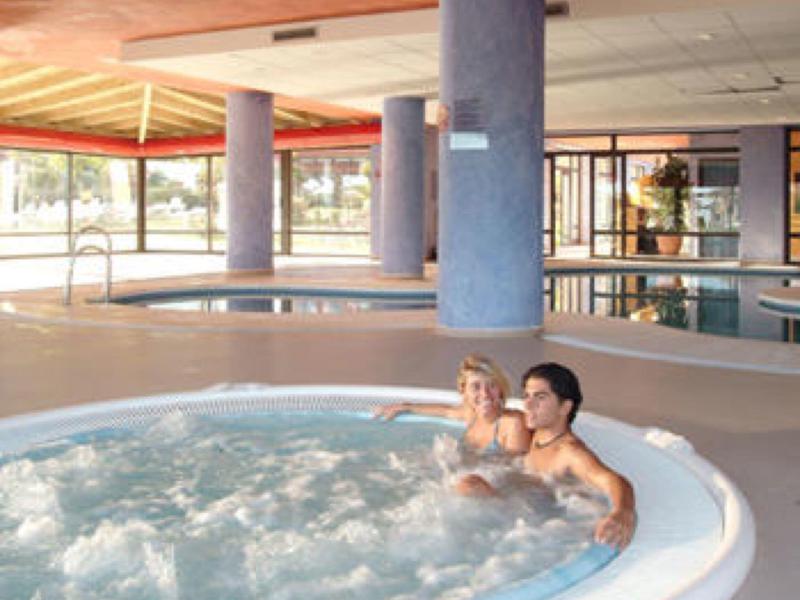 Dos personas se relajan en un jacuzzi dentro de un área interior moderna de un hotel con grandes ventanas de vidrio.