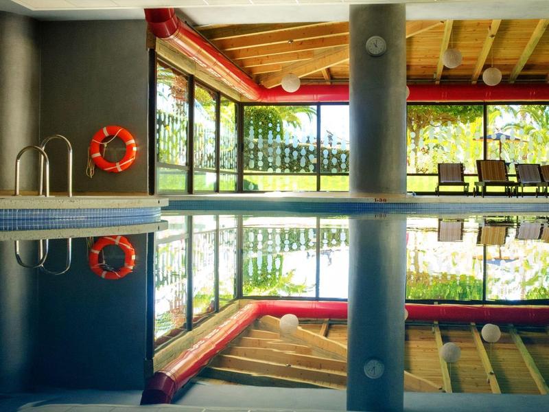 Piscina interior con columnas y grandes ventanales que dan a un paisaje verde exterior.