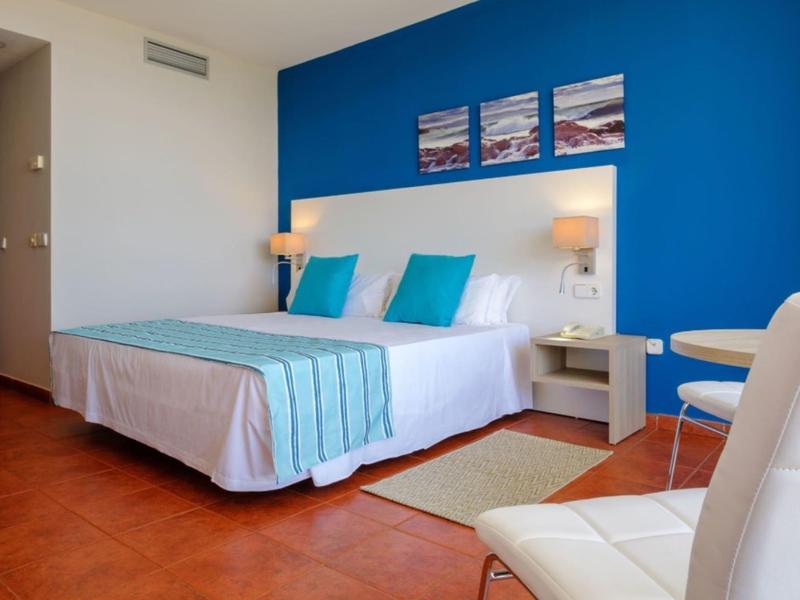 Habitación de hotel moderna con acento azul, cama doble y zona de asientos con sillas y mesitas.