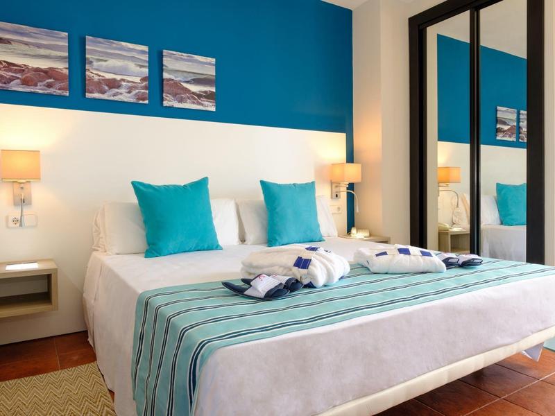 Habitación de hotel moderna con cama doble, almohadas turquesas y cuadros sobre la cabecera.