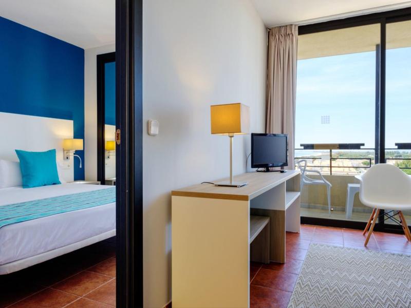 Habitación de hotel moderna con cama doble, escritorio, televisor y balcón con vista.