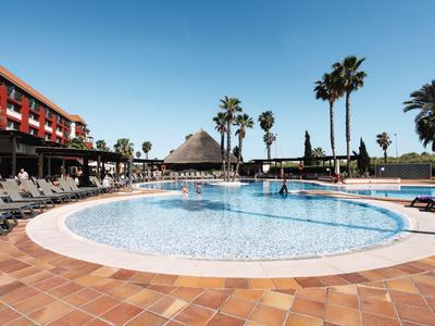 Grande piscina rotonda con lettini e palme sotto un cielo sereno in un hotel.