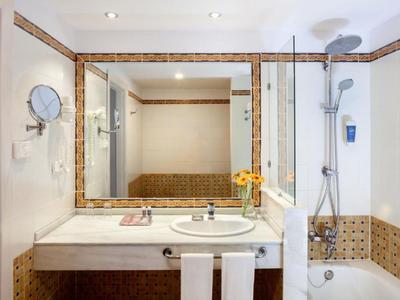 Bagno luminoso con grande specchio, lavabo e vasca con doccia.