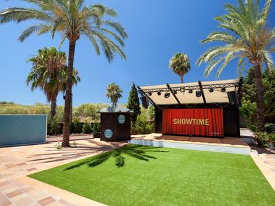 Palco all'aperto con palme e prato verde sotto un cielo limpido