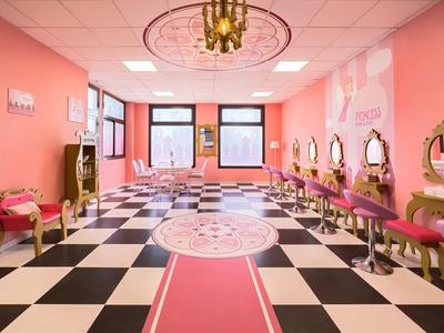 Salone di parrucchiere con pareti rosa, pavimento a scacchi bianco e nero e più sedie rosse.