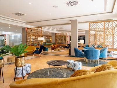 Area lounge dell'hotel moderna con divani gialli, poltrone blu e dettagli in legno.