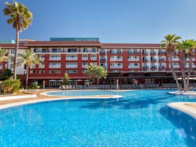Grande piscina all'aperto davanti a un edificio alberghiero pluripiano con palme e cielo blu.